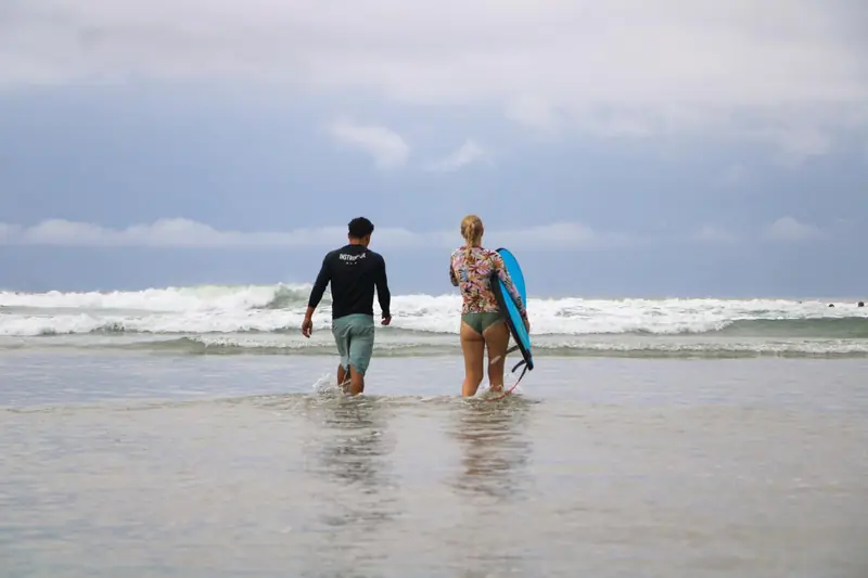 Weyser y una alumna entrando juntos al mar con sus tablas
