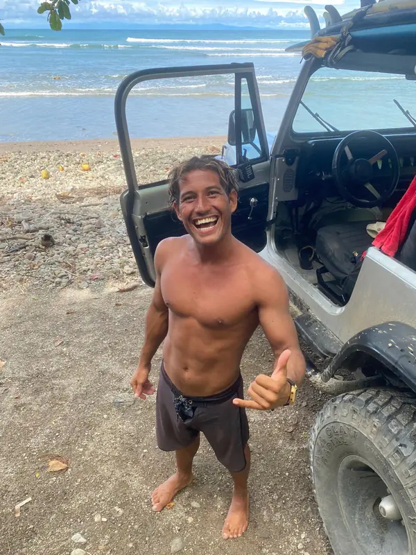 Weyser riéndose y haciendo shaka junto a su jeep en la playa